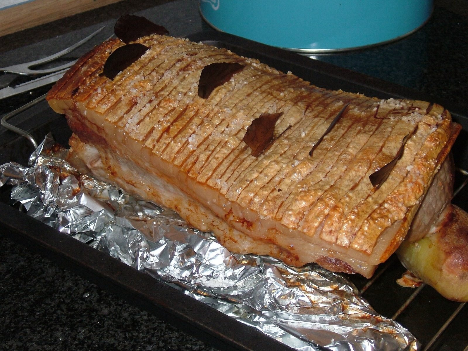 Flæskesteg à la couenne incisée et croustillante, garni de feuilles de laurier, sur une grille de four