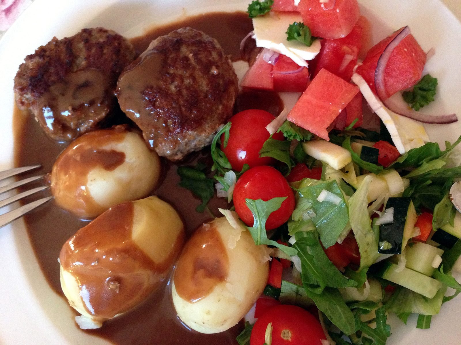 Frikadeller med kartofler, brun sovs og farverig salat på en tallerken